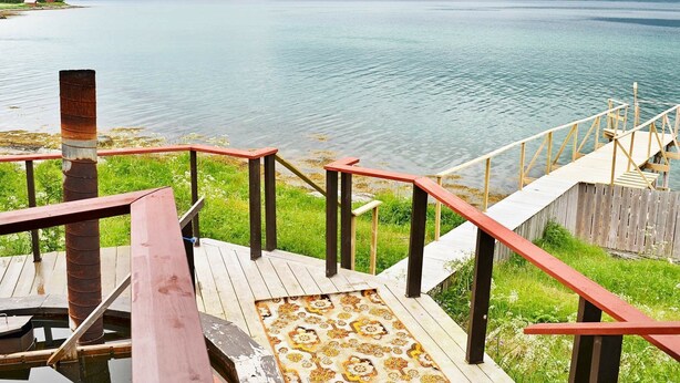 A wooden deck with a patterned rug leading to a lake with mountains in the background. - 6 Person Holiday Home in Hamnvik (Ibestad)