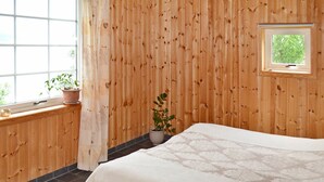 A room with wooden panel walls, a bed with a patterned bedspread, a window with a view of greenery, and two potted plants on the windowsill. - 6 Person Holiday Home in Hamnvik (Ibestad)