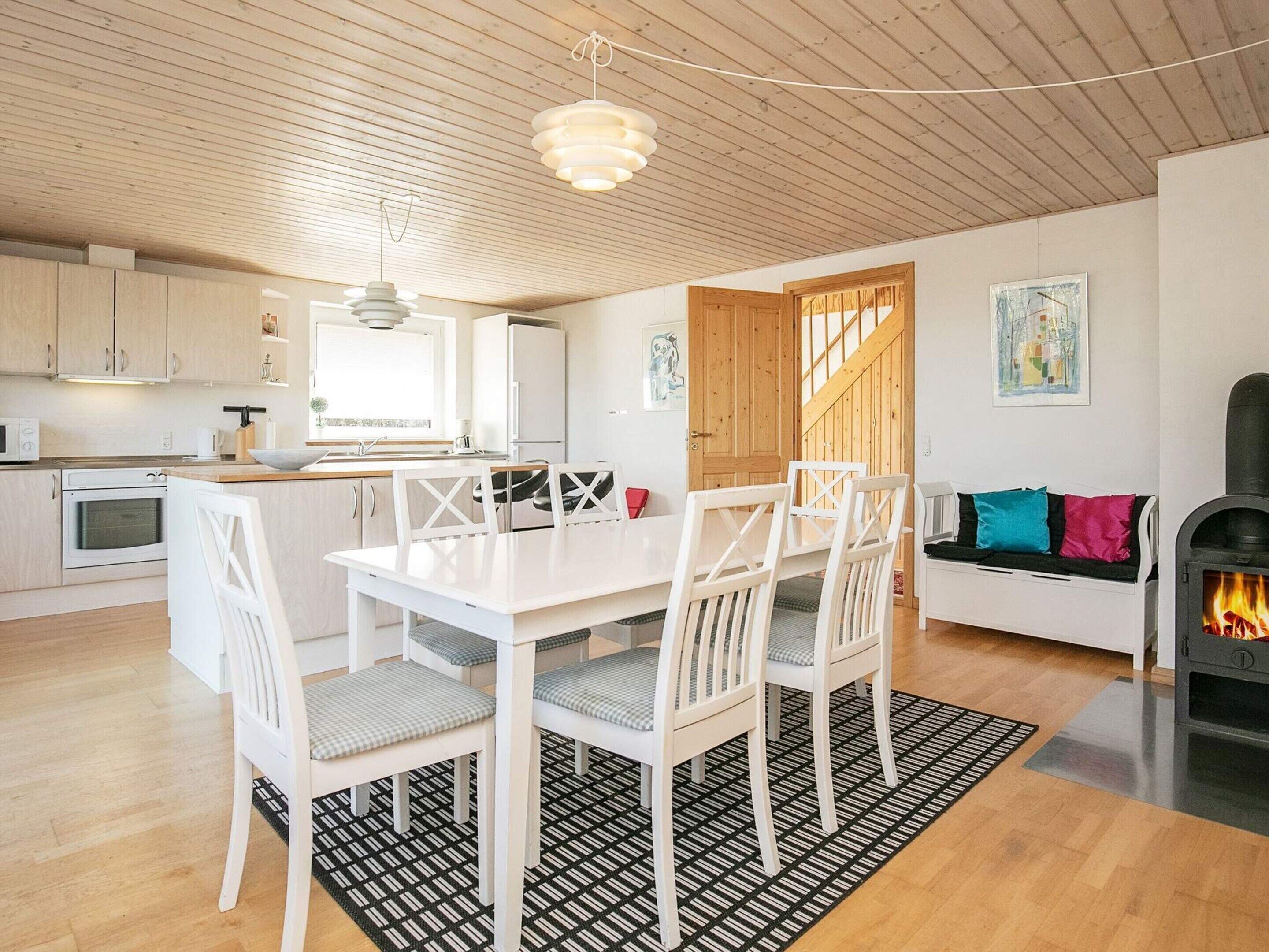 A modern kitchen with white cabinetry, a dining area with a white table and chairs, and a cozy seating area with a sofa and cushions.