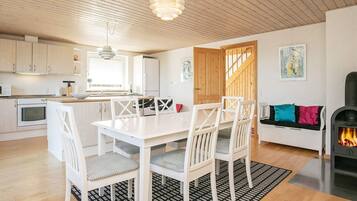 A modern kitchen with white cabinetry, a dining area with a white table and chairs, and a cozy seating area with a sofa and cushions.