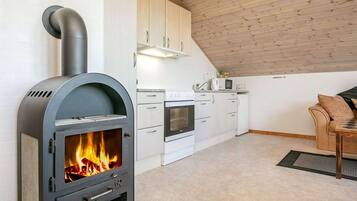 Una cocina moderna con estufa de leña, armarios blancos y un comedor con mesa y sillas.