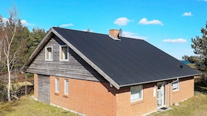 Une maison de plain-pied en briques, avec un toit sombre, deux fenêtres et une cheminée.