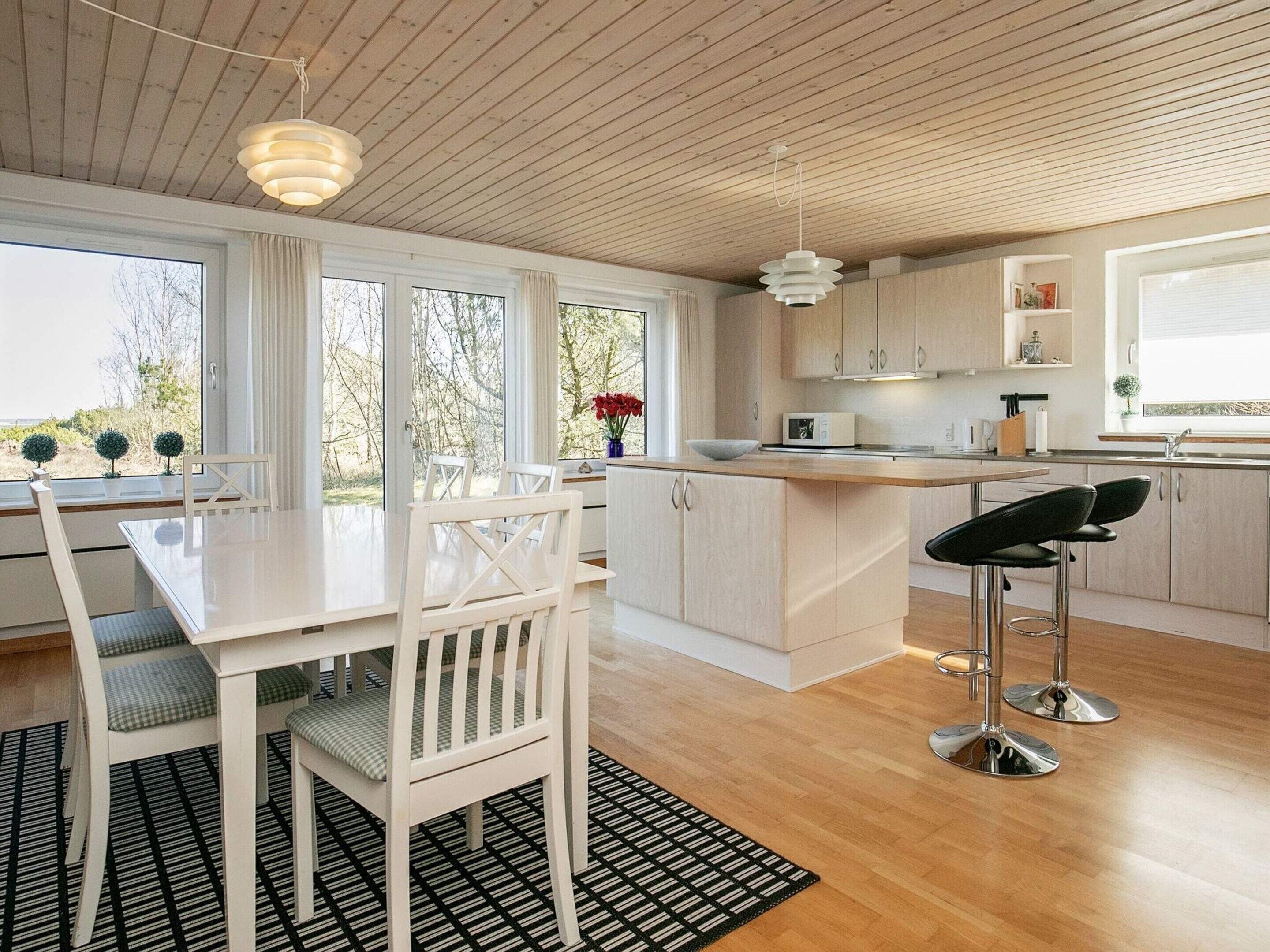 Une cuisine moderne avec des meubles blancs, une table à manger avec des chaises et un coin bar avec des tabourets.