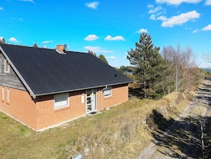 A single-story brick house with a dark roof, a visible chimney, and a small front yard with grass and a pathway leading to the house.