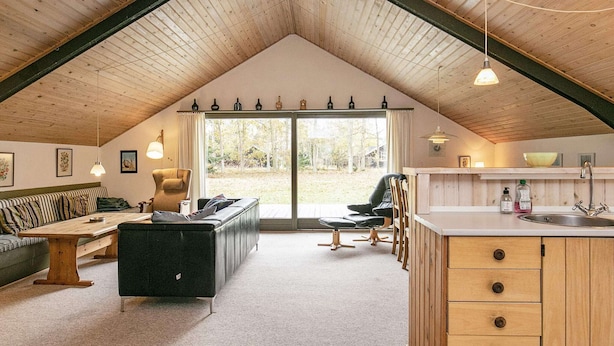 Ein gemütliches Loft mit schrägverdeckter Decke, Essbereich, Sofa, schwarzem Ledergestell, Küchenzeile mit Holzschränken und einem großen Schiebeglastür zu einem Außenbereich.