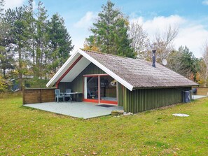 A small, single-story building with a sloped roof, a covered patio area with two chairs, and a large sliding glass door. - 5 Person Holiday Home in Martofte (Martofte)