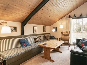 A cozy room with a wooden ceiling, a striped sofa, a wooden table, and a view of trees through a window. - 5 Person Holiday Home in Martofte (Martofte)