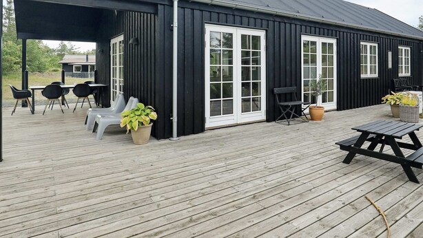 Un bâtiment noir avec des fenêtres à encadrement blanc et un espace extérieur abrité, aménagé avec des chaises et des tables.