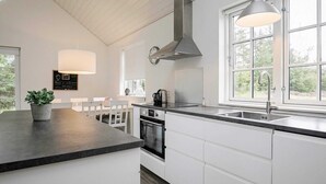 Une cuisine moderne avec des meubles blancs, un plan de travail foncé, une hotte en acier inoxydable et une fenêtre qui laisse entrer la lumière naturelle.