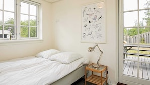 Une chambre à coucher comprenant un lit, une lampe de chevet, une fenêtre et une porte donnant sur une terrasse extérieure.