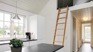Une cuisine avec un plan de travail noir, une plante en pot, une machine à café et une échelle en bois appuyée contre le mur.