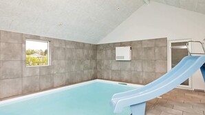 A modern indoor swimming pool with a blue slide, grey tiled walls, and a ceiling with recessed lighting. - Luxury Retreat With Pool - By Traum Ferienwohnungen (Gørlev)