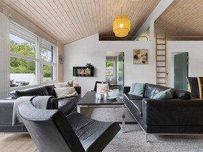 A modern living room with leather sofas, a dining table, and a TV mounted on the wall. - 5 Star Holiday Home in Ebeltoft (Ebeltoft)