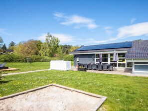 A building with a solar panel roof, outdoor seating, and a grassy yard.