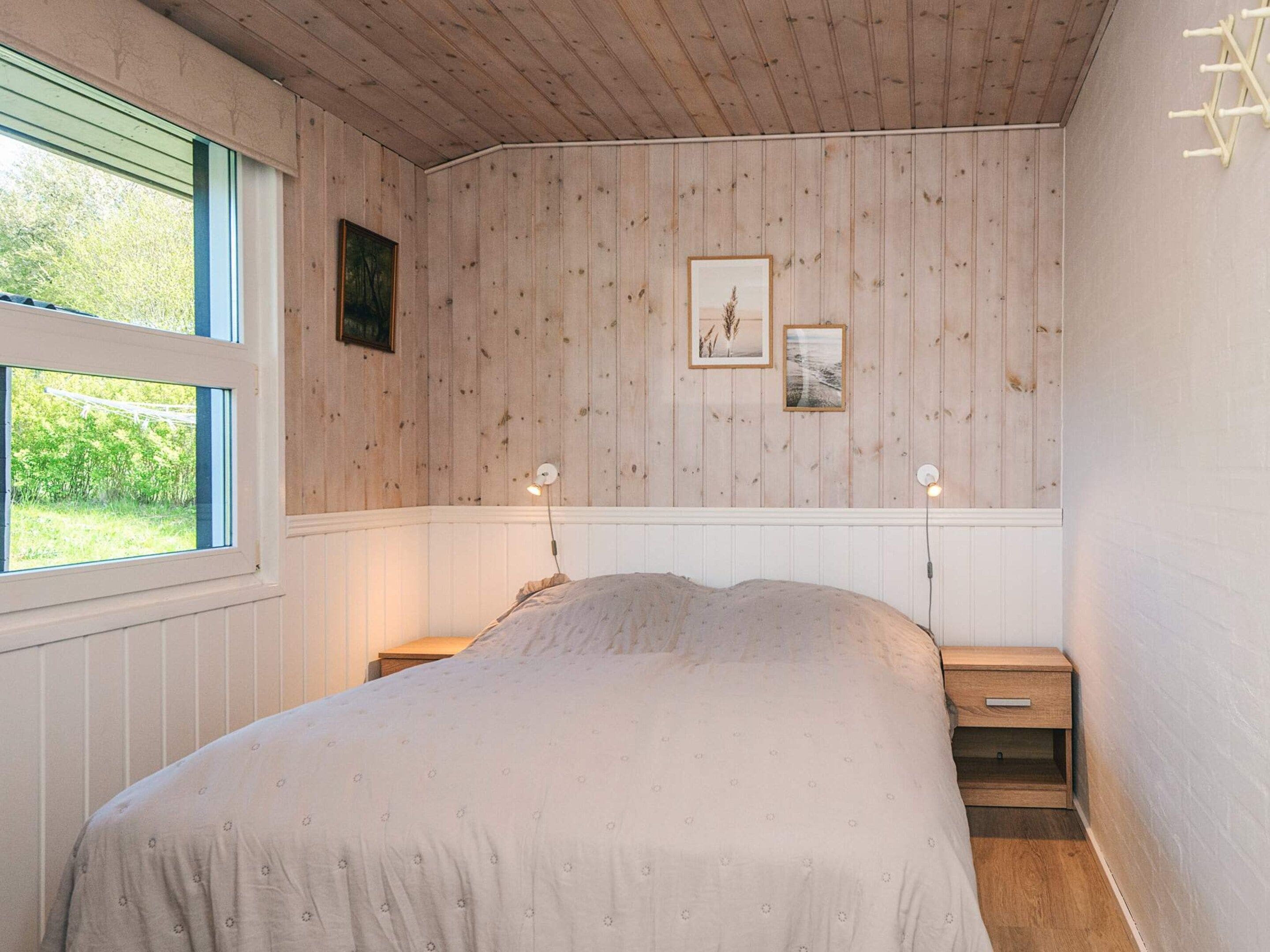 A bedroom with a bed, two bedside tables, a window, and wooden panel walls.
