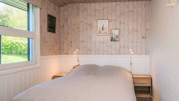A bedroom with a bed, two bedside tables, a window, and wooden panel walls.