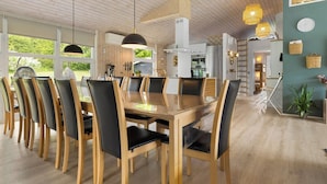 A modern dining area with a wooden table and chairs, large windows, and a kitchen in the background. - 14 Person Holiday Home in Ebeltoft-by Traum (Ebeltoft)