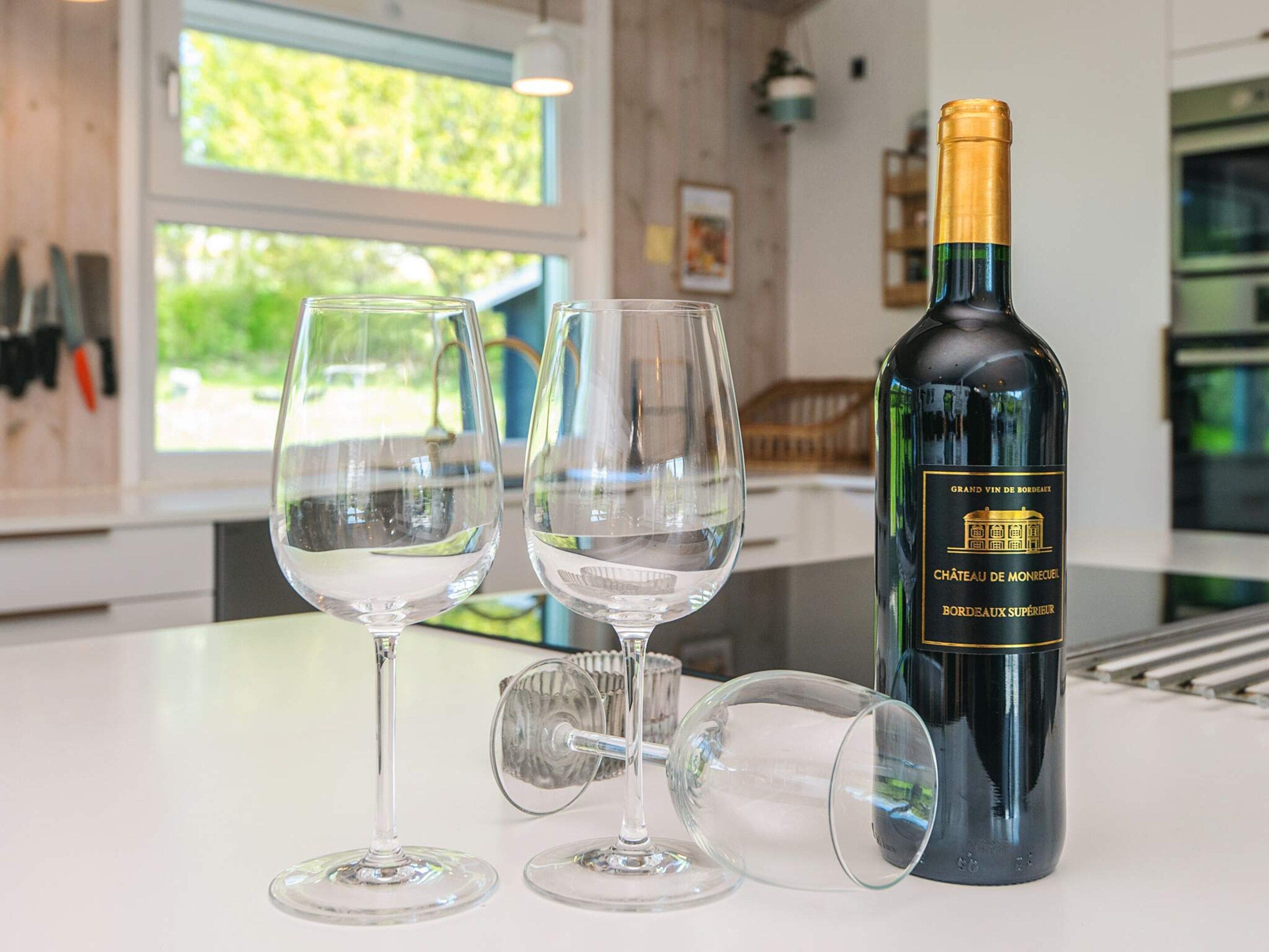 Uma garrafa de vinho, duas taças e um suporte para taça em cima de uma mesa.