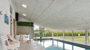 An indoor swimming pool with a view of the outdoors, a bench, and a wall-mounted air conditioner. - 14 Person Holiday Home in Ebeltoft-by Traum (Ebeltoft)