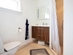 Une salle de bain avec des toilettes, un lavabo avec un miroir, une serviette accrochée au mur et un rideau de douche.