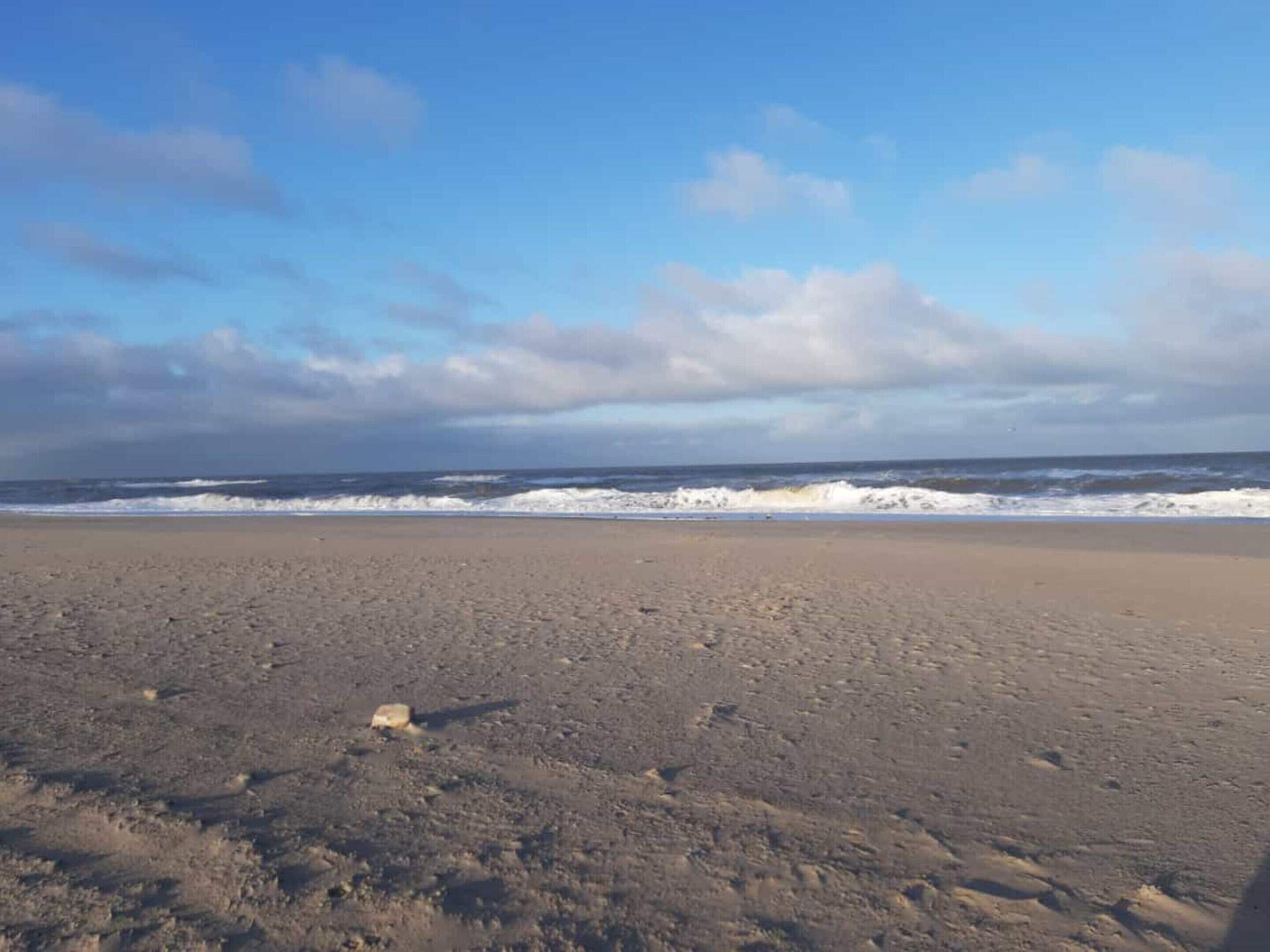 A beach with waves, a clear sky, and a few scattered rocks.