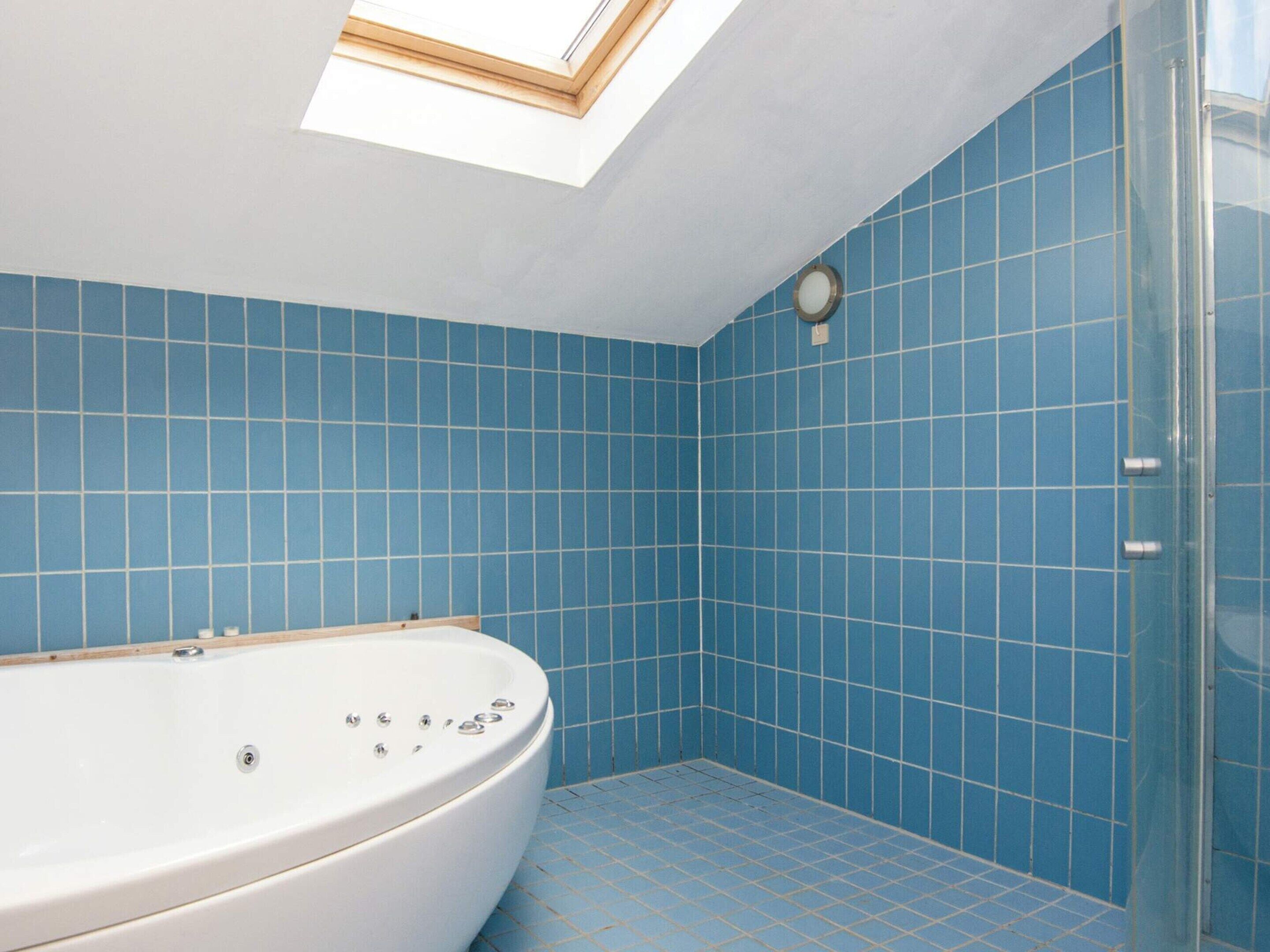 A bathroom with a freestanding bathtub, blue tiled walls, and a skylight.