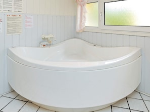Una bañera grande y blanca en un baño con paredes blancas y piso de baldosas.