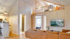 Un intérieur moderne avec un mur lambrissé en bois, un canapé en cuir, un escalier et un téléviseur fixé au mur.