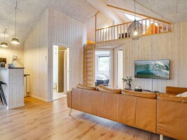 Un interior moderno con un panel de madera, un sofá de cuero, una escalera y un televisor montado.