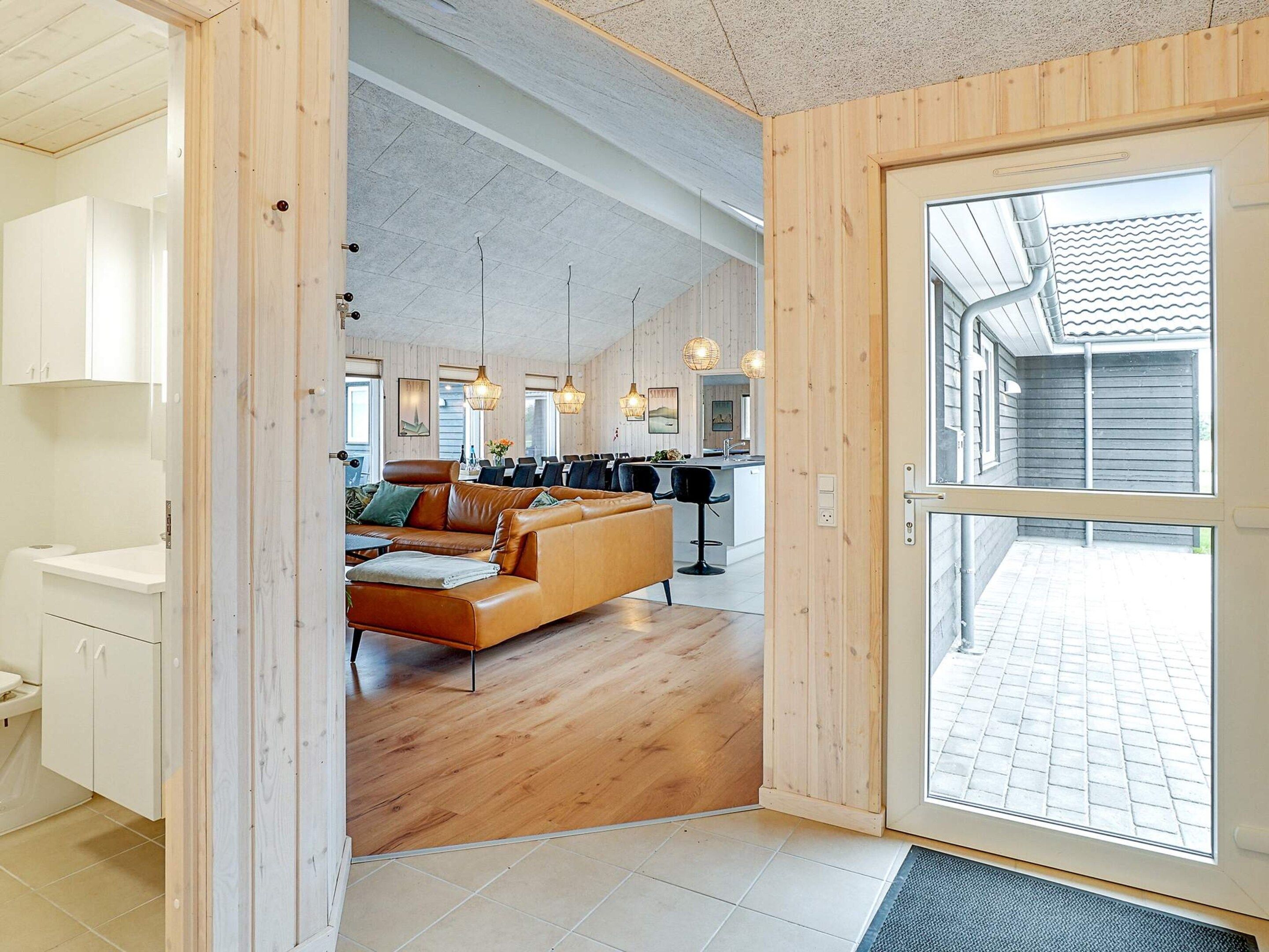 Un interior moderno con piso de madera, un sofá de cuero y un comedor con sillas y lámparas colgantes.