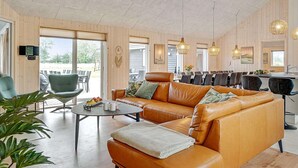 Un vaste espace de vie comprenant un canapé en cuir, une table à manger et des chaises, des murs en bois et de grandes fenêtres.