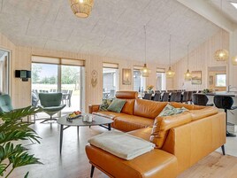 Un amplio salón con sofá de cuero, mesa de comedor y sillas, paredes de madera y ventanas grandes.