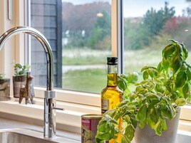 Una cocina con un grifo de acero inoxidable, una planta de albahaca, una lata de aceite de oliva y una botella de aceite de oliva.