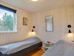A room with two single beds, a small bedside table with a book, a wall-mounted mirror, and a window with a view of trees. - Spacious Holiday Home in Grenå near Sea (Grenaa)