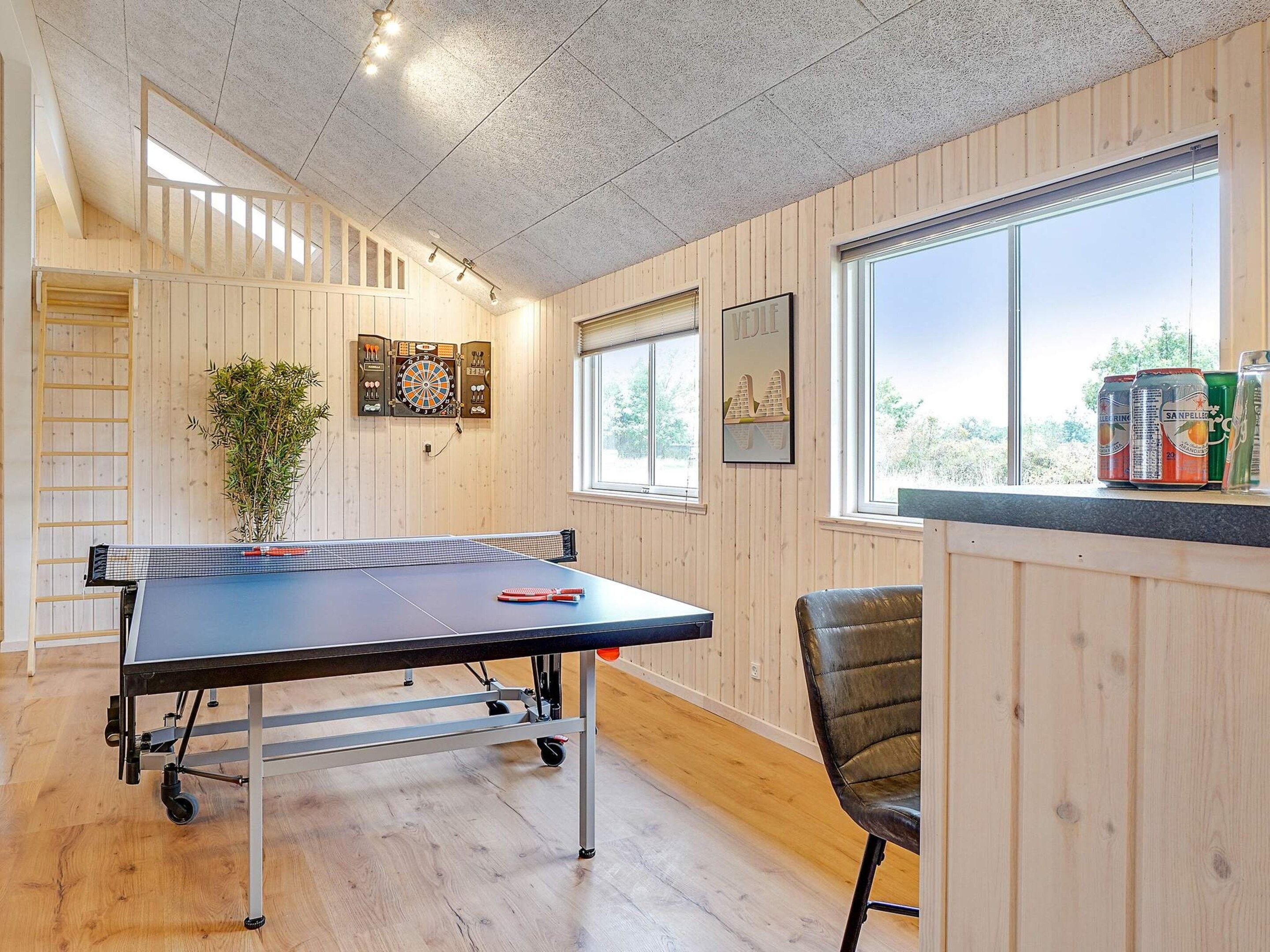 Una mesa de ping pong en una habitación con paredes de madera, una ventana y un dardo.