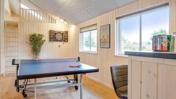 Una mesa de ping pong en una habitación con paredes de madera, una ventana y un dardo.