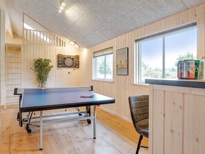 Une table de ping-pong dans une pièce aux murs en bois, avec une fenêtre et un jeu de fléchettes.