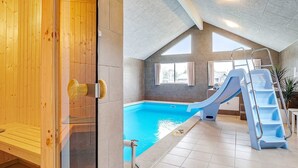 Une piscine avec un toboggan et une échelle, des murs en bois et un sol carrelé.