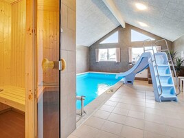 Una piscina con tobogán y escalera, paredes de madera y suelo de baldosas.