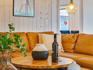 Un salon chaleureux avec un canapé en cuir marron, une table basse ronde en bois, une bouteille de vin, un verre et un vase contenant des plantes vertes.