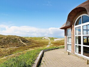 Ein Gebäude mit Ziegelaußenwand und großen Fenstern, mit Blick auf eine hügelige Landschaft unter blauem Himmel.