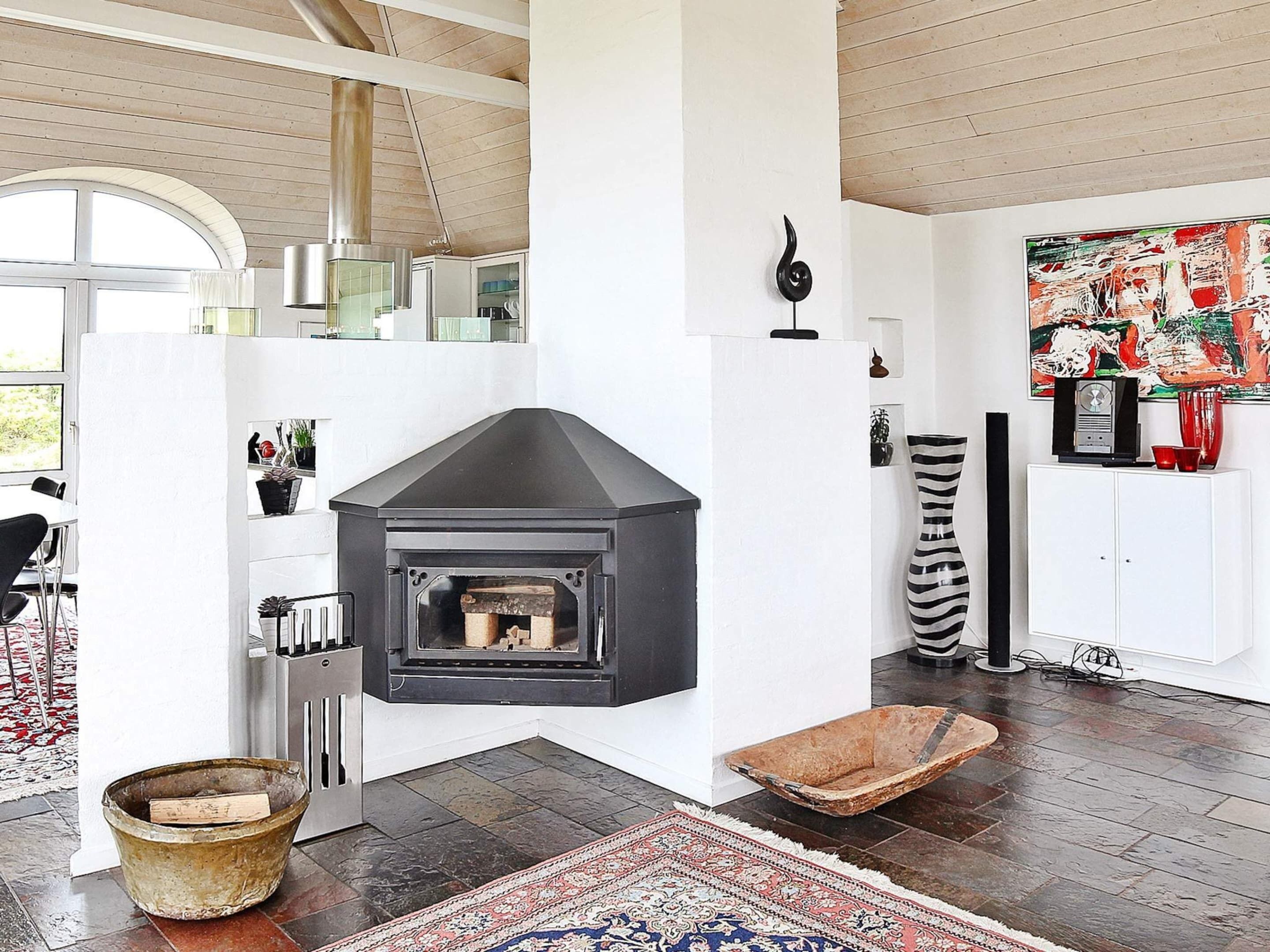 Una sala de estar moderna con una chimenea negra, un ventanal grande y un cuadro abstracto colorido en la pared.