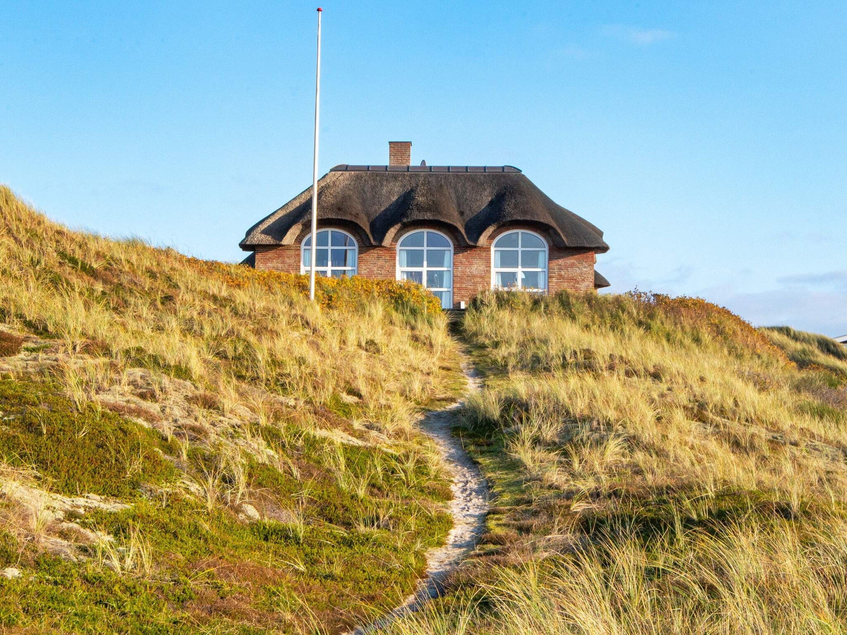 A house with a thatched roof, situated on a grassy hill with a clear sky.