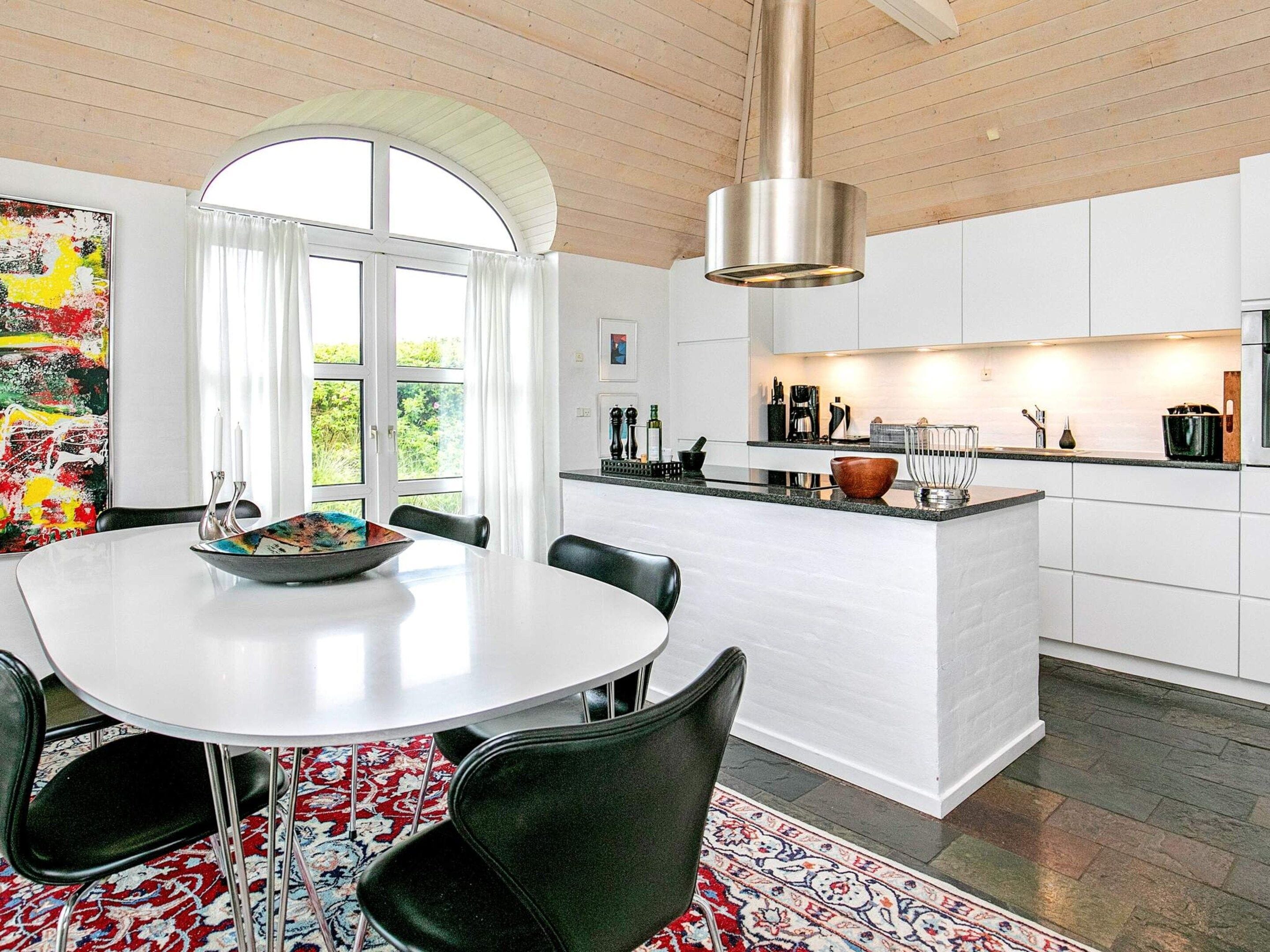 A modern kitchen with white cabinetry, a central island, and a dining area with a round table and chairs.