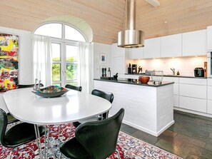 Une cuisine moderne avec des meubles blancs, un îlot central et un coin repas comprenant une table ronde et des chaises.