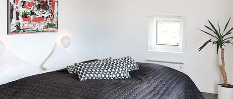 A bedroom with a large bed, a potted plant, a window, and a wall-mounted artwork.