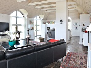 Ett modernt vardagsrum med en svart lädersoffa, en turkos vas med blommor, en öppen spis och en köksdel.
