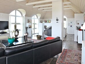 Un interior modern amb un sofà de cuir negre, un vas de ceràmica color turquesa amb flors, una zona de cuina i un espai de menjador.