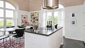 A modern kitchen with a central island, large windows, and contemporary artwork. - 5 Star Holiday Home in Ringkobing (Ringkobing)