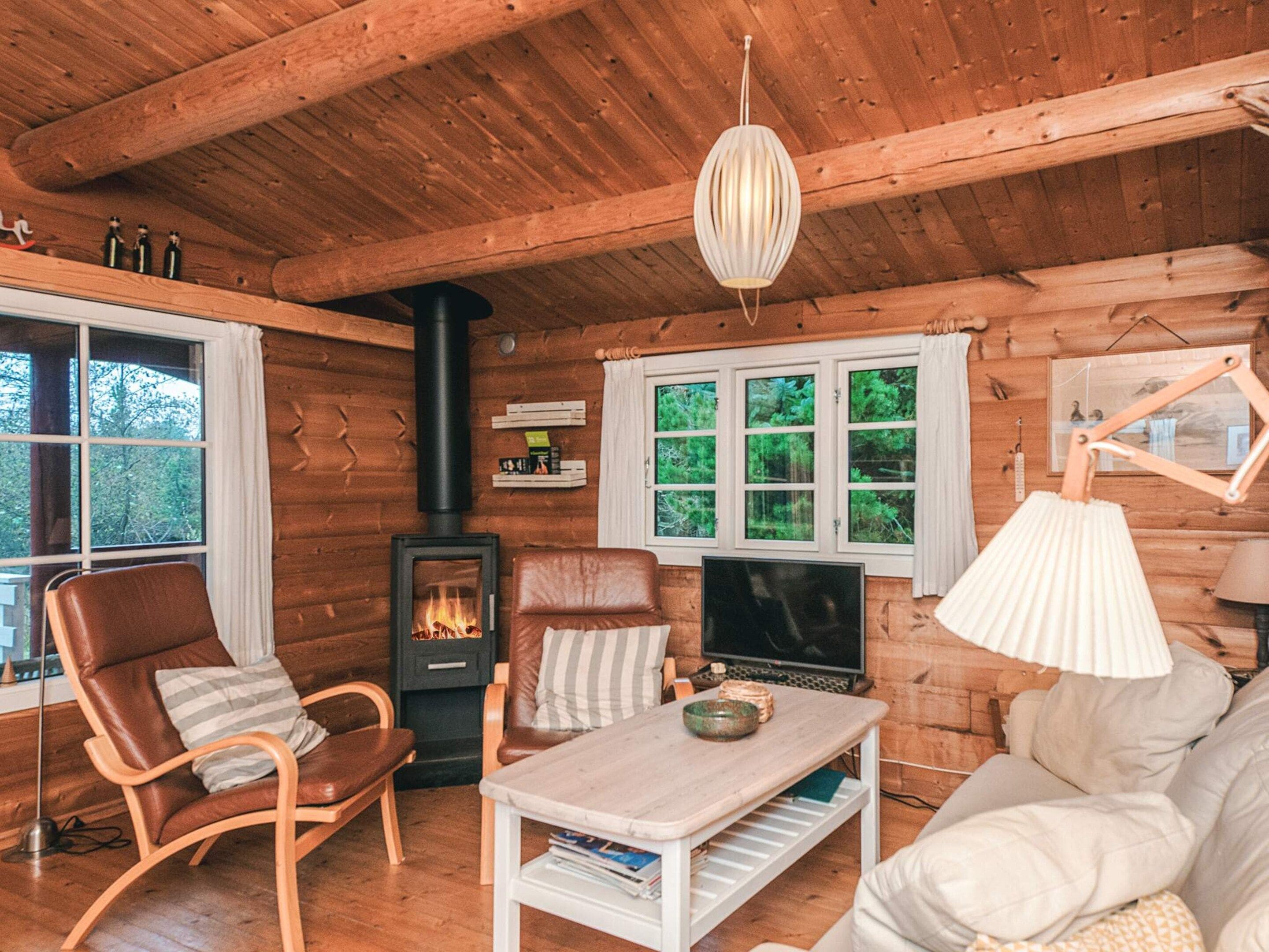 A cozy cabin interior with a fireplace, leather chairs, a television, and a wooden ceiling.